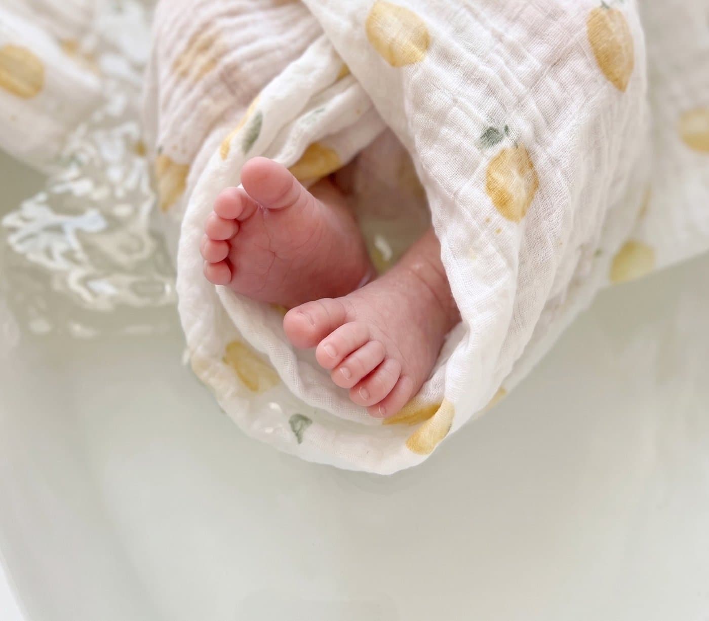 Pieds de bébé enveloppés dans un lange en double gaze de coton à motif citrons, pendant le bain